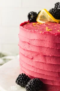 a lemon cake frosted with blackberry buttercream and topped with lemon zest, a twist of lemon, and fresh blackberries