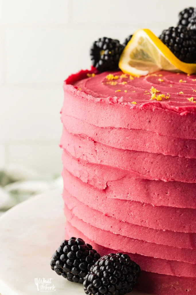 a lemon cake frosted with blackberry buttercream and topped with lemon zest, a twist of lemon, and fresh blackberries