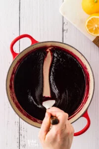 overhead shot of thickend blackberry cake filling in a red Le Creuset dutch oven with a spatula