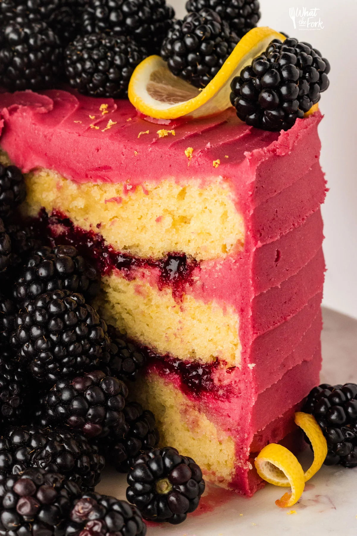 a slice of lemon black berry cake being cut to show the layers of blackberry cake filling