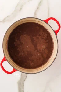 ingredients to make gluten free chocolate pudding whisked together in a white and red Dutch oven ready to be cooked