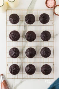 baked gluten free chocolate cupcakes cooking on a gold wire rack on top of a white marble surface