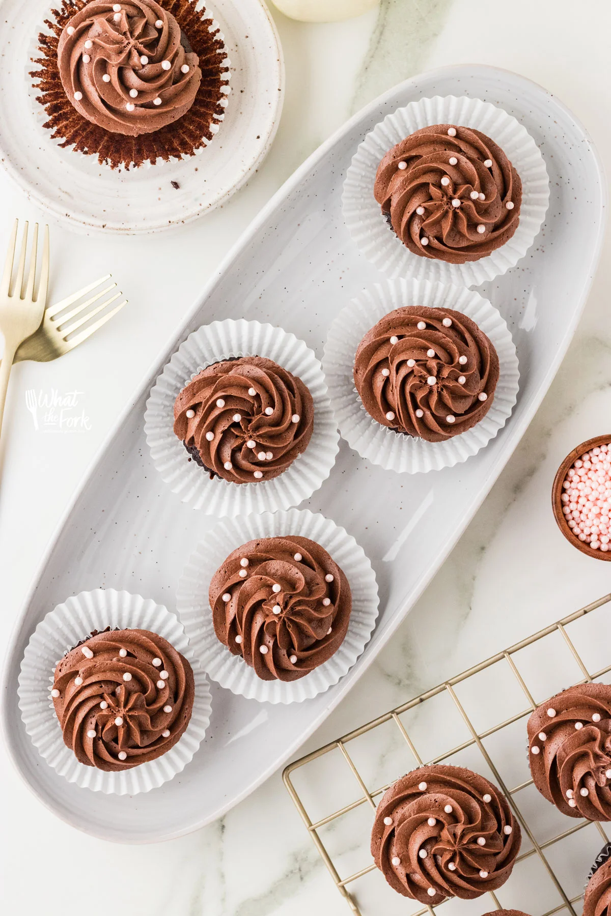 overhead shot of gluten free chocolate cupcakes frosted with chocolate buttercream frosting on a white oval platter.