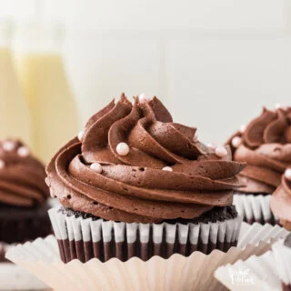 baked Moist and Rich Gluten Free Chocolate Cupcakes in white paper liners frosted with chocolate frosting and decorated with small pearl sprinkles