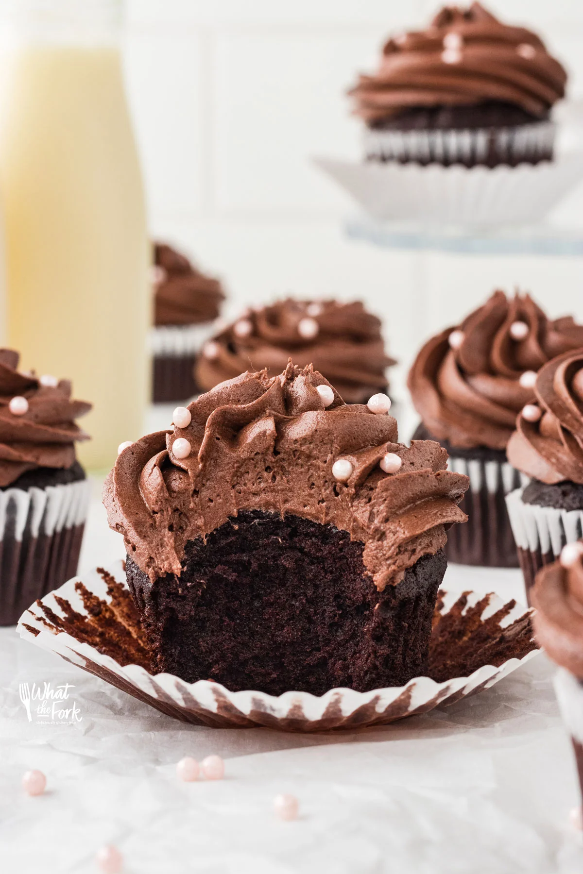 a gluten free chocolate cupcake with chocolate frosting in an opened white liner with a bite taken out