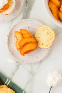 overhead shot of a gluten free drop biscuit split in half with macerated peaches on one half served on a round white plate
