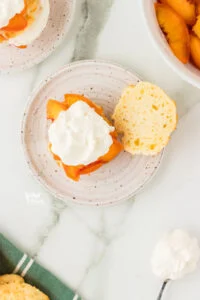 overhead shot of a gluten free drop biscuit split in half with macerated peaches and whipped cream on one half served on a round white plate