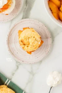 overhead shot of a gluten free peach shortcake on a round white plate topped with more macerated peaches