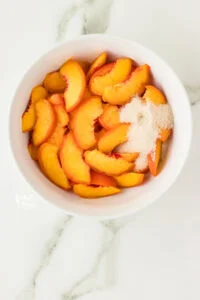 sliced peaches in a white bowl with granulated sugar and lime juice to make macerated peaches