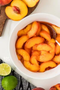 sliced peaches mixed together in a white bowl with granulated sugar and lime juice to make macerated peaches