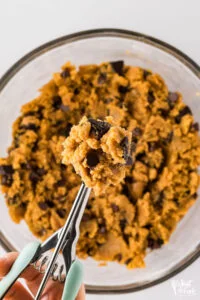 a cookie scoop with a scoop filled with gluten free peanut butter chocolate chip cookie dough held over the bowl of cookie dough