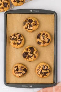six baked gluten free chocolate chip peanut butter cup cookies on a brown parchment paper lined cookie sheet