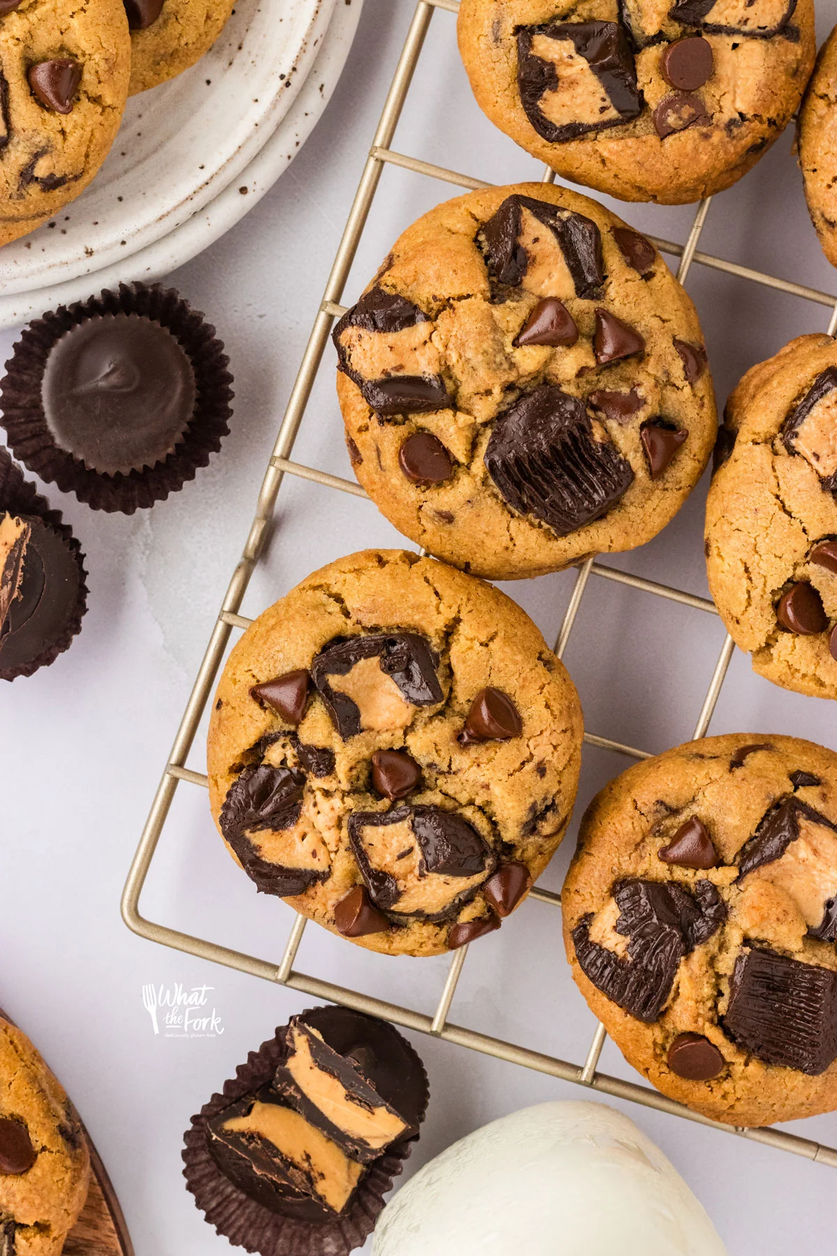 Loaded Gluten Free Peanut Butter Chocolate Chip Cookies cooling on a wire rack with peanut butter cups surrounding