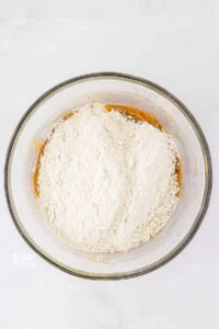 gluten free flour blend and other dry ingredients added to the top of the wet ingredients to make gluten free peanut butter cookies