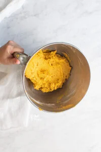 pumpkin cookie dough in a silver stand mixer bowl being held by a hand