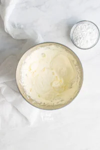 Cream Cheese Frosting in a large silver bowl with powdered sugar on the side