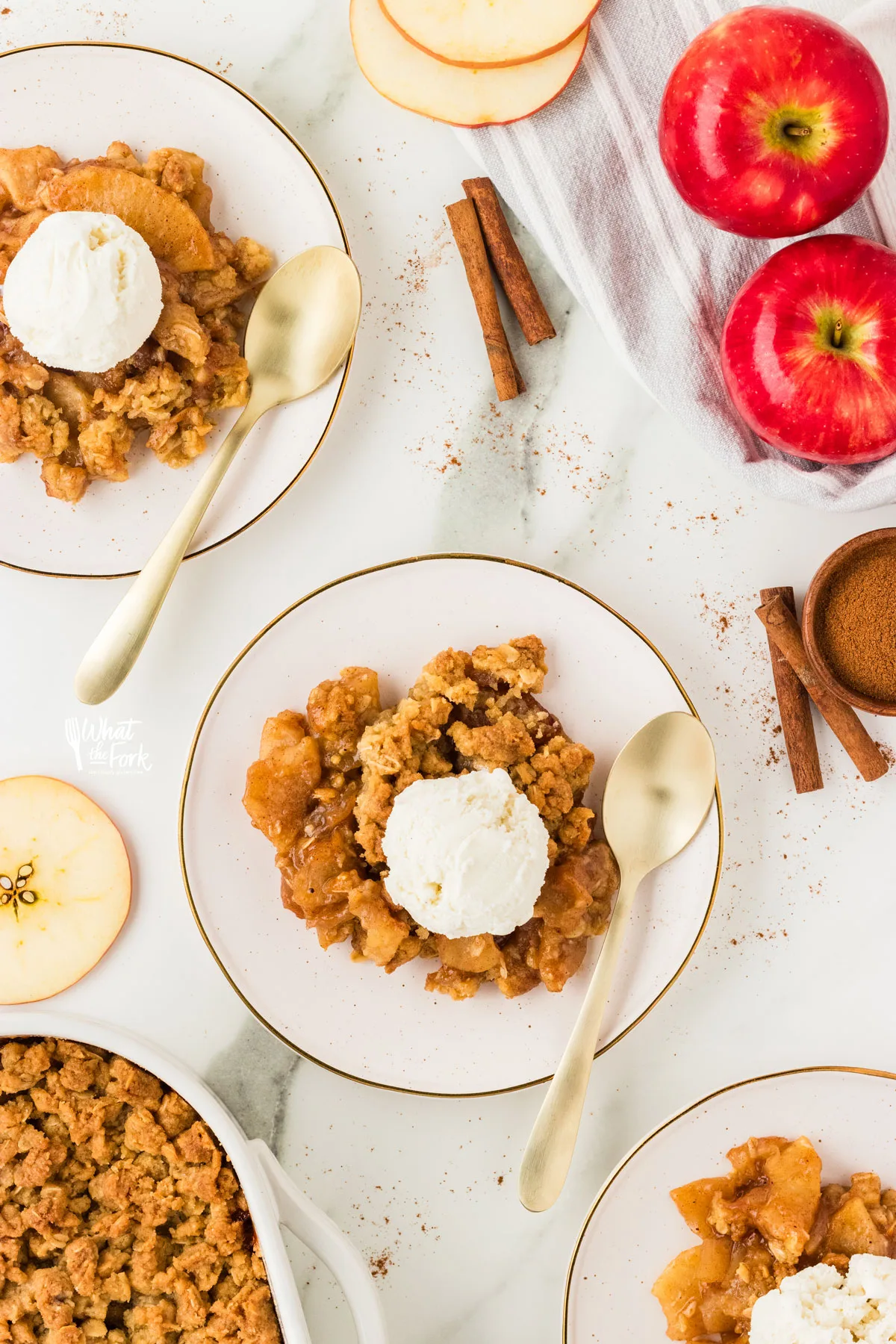 overhead shot of gluten free apple crisp plated on 3 plates with gold spoons and topped with vanilla ice cream