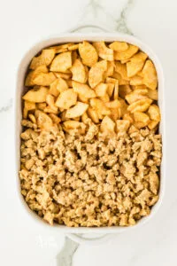 gluten free crisp topping is spread over half the apples in a white 9x13 baking dish