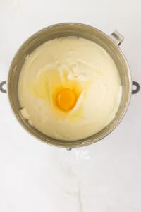 an egg added to cream cheese and sugar in a stand mixer bowl