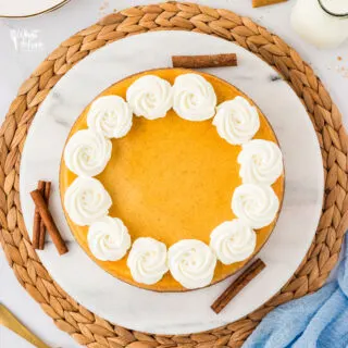 overhead shot of a Layered Pumpkin Cheesecake made with a Gluten Free Crust and decorated with dollops of whipped cream served on a white marble platter on a rattan charger.