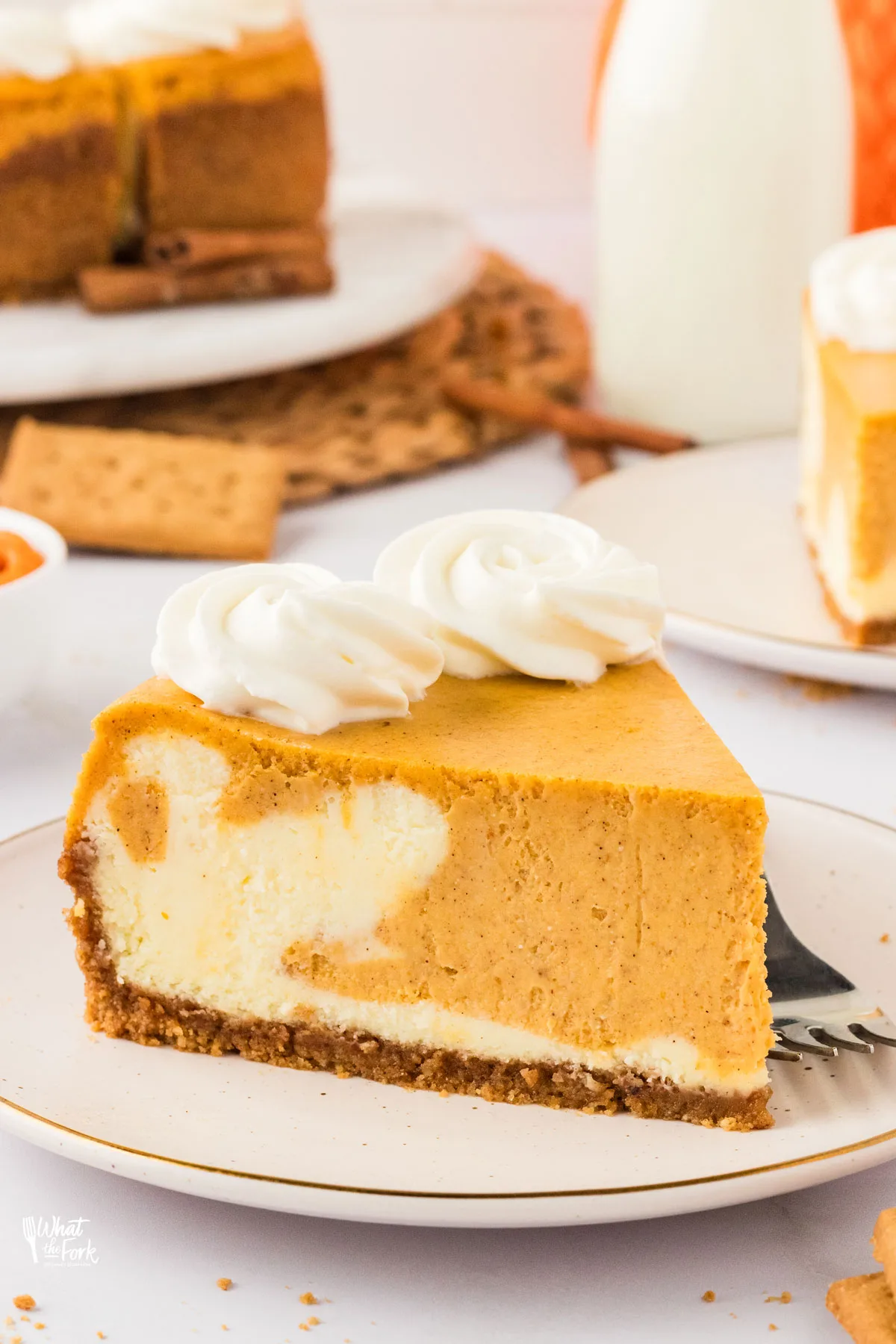 a slice of marbled and Layered Pumpkin Cheesecake with a Gluten Free Crust on a small round white plate with a silver fork on the side