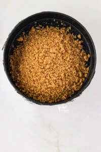 gluten free graham cracker crust with pecans poured into a black springform pan