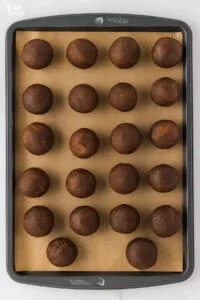 gluten free ginger cookie dough balls rolled on a brown parchment paper lined cookie sheet