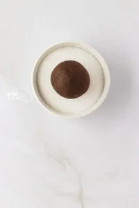 a ball of gluten free ginger cookie dough sitting on top of a small white bowl filled with sugar