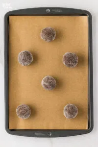 gluten free ginger cookie dough rolled in sugar and placed on a brown parchment paper lined cookie sheet