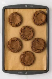 6 gluten free ginger cookies baked on a brown parchment paper lined cookie sheet