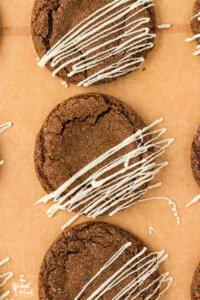 overhead shot of 3 gluten free ginger cookies on brown parchment paper that have been drizzled with white chocolate