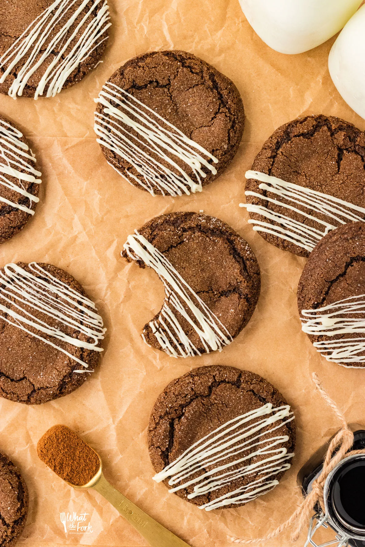 overhead shot of baked gluten free ginger cookies drizzled with white chocolate on top of brown parchment paper. One cookie has a bite taken from it.
