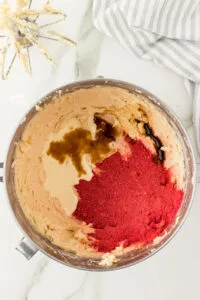 whipped vanilla frosting with vanilla extract, heavy cream, and powdered freeze dried strawberries in a large silver stand mixer bowl