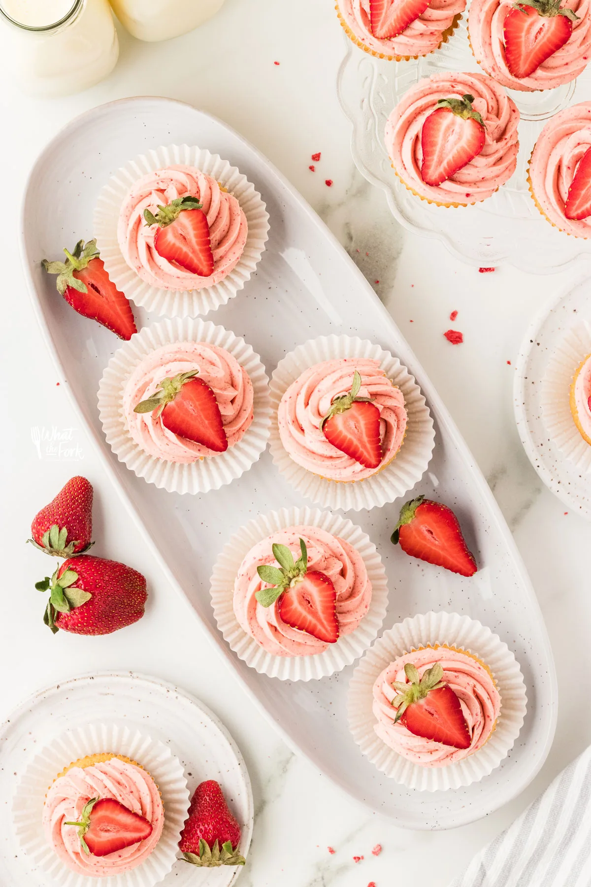 overhead shot of cupcakes on an oval white plater frosted with a swirl of strawberry frosting and topped with half of a strawberry