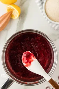 strawberry cake filling cooked in a silver saucepan with some on a white silicone spatula to show how thickened it is.