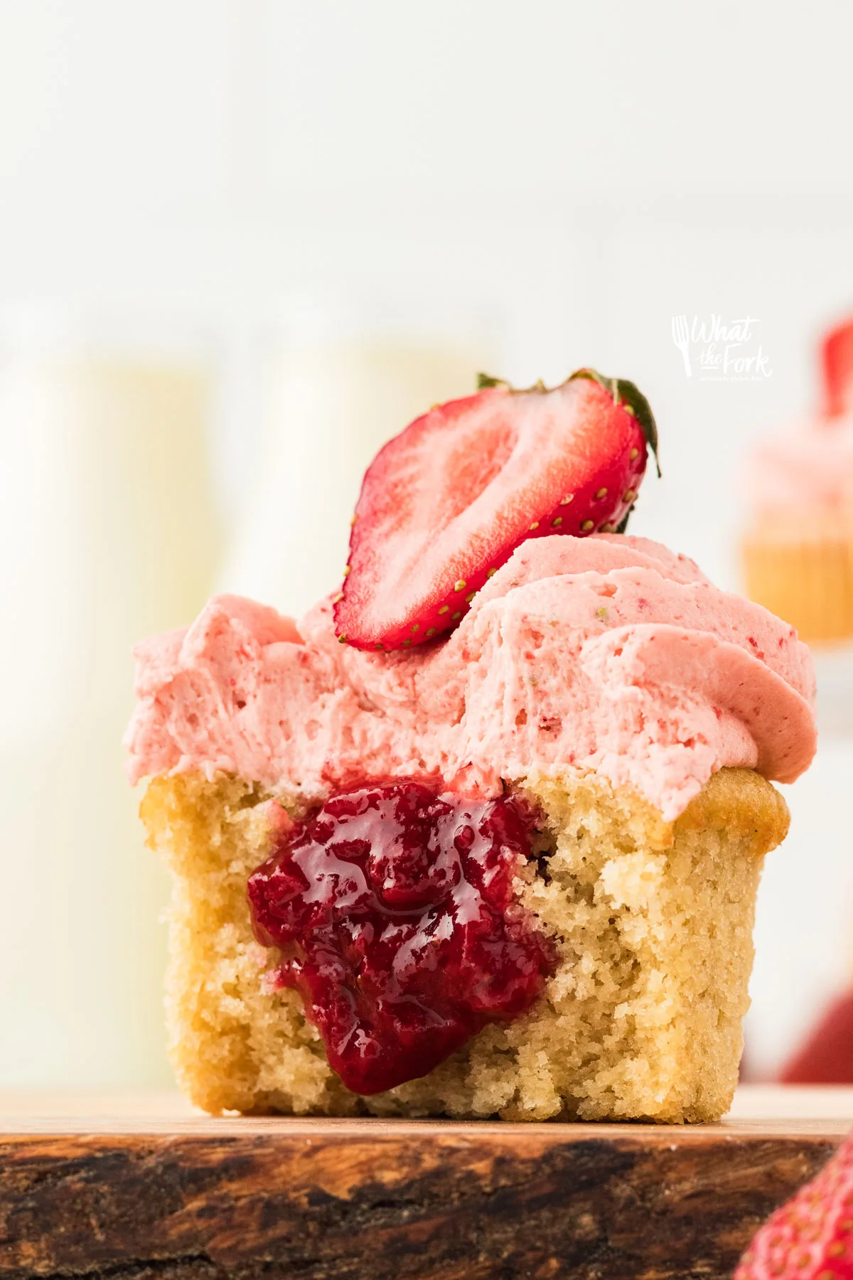 a gluten free vanilla cupcake filled with an easy 3-Ingredient Strawberry Cake Filling. The cupcake is cut open to show the filling and is topped with strawberry frosting and half of a fresh strawberry.