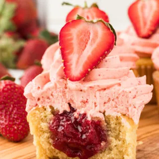 a gluten free vanilla cupcake filled with an easy 3-Ingredient Strawberry Cake Filling. The cupcake is cut open to show the filling and is topped with strawberry frosting and half of a fresh strawberry.