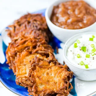 Deep golden brown, fried gluten free Latkes on a blue and white plate with small bowls of sour cream and applesauce on the side