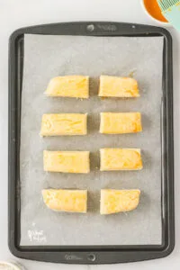 unbaked gluten free pretzel biscuits on a parchment paper lined baking sheet topped with an egg wash and pretzel salt