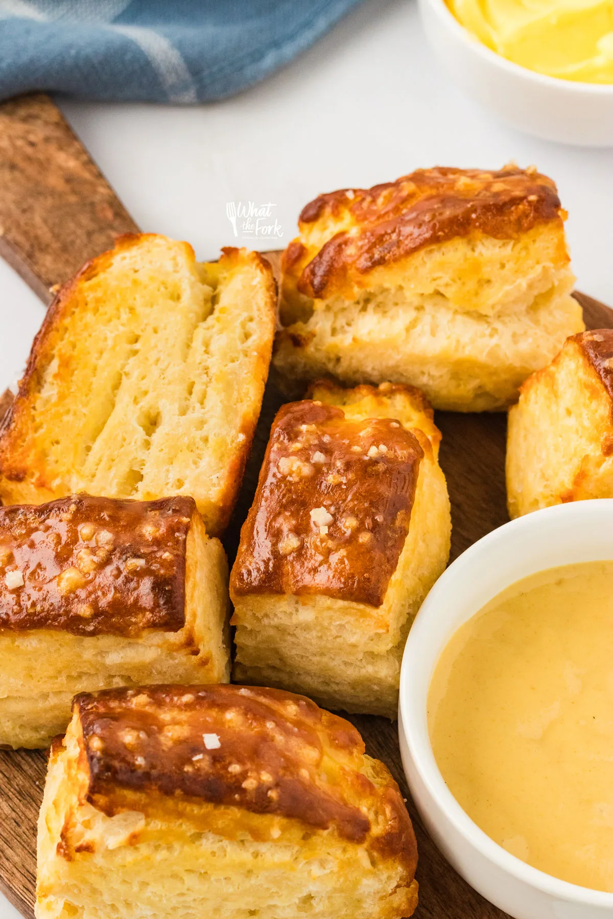 Buttery Prezel Biscuits on a round wood serving platter with a handle with a small white bowl of honey mustard