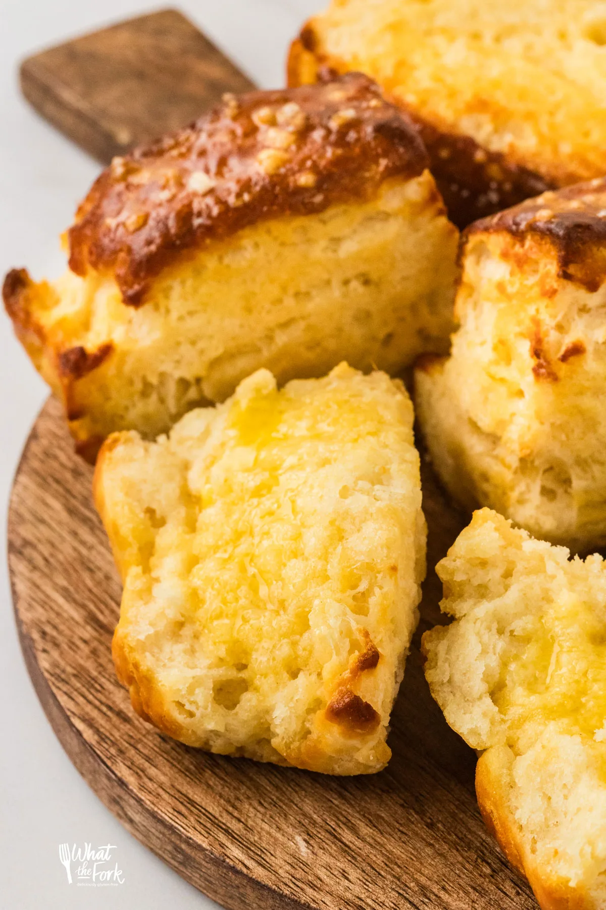 Buttery Prezel Biscuits made with Gluten Free Flour split open and smeared with butter on top of a round wood serving platter