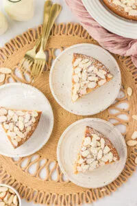 three slices of almond flour cake on small round white plates on top of a wicker charger