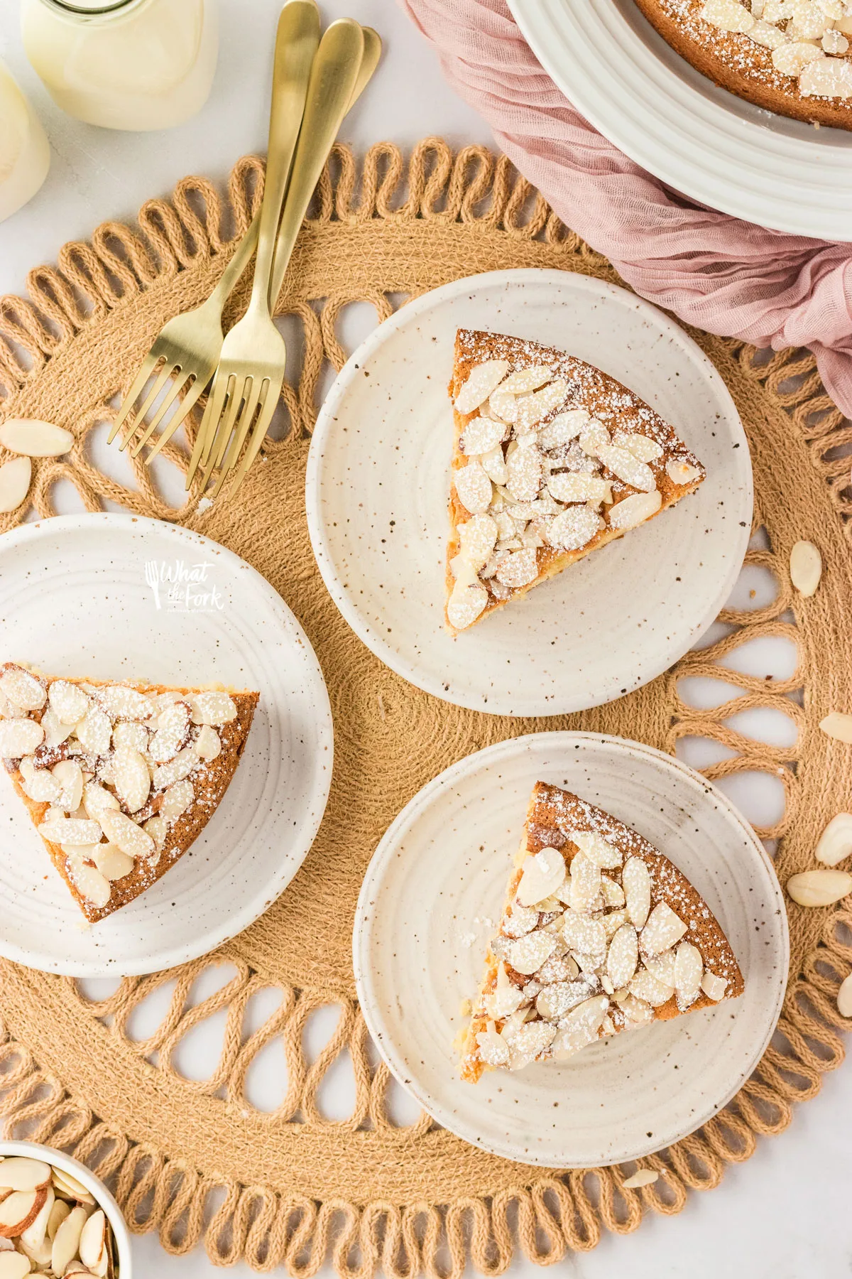three slices of almond flour cake on small round white plates on top of a wicker charger
