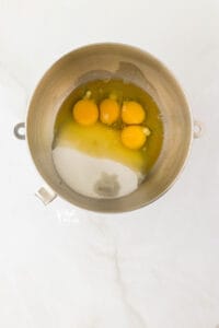 whole eggs out of the shell, granulated sugar, and almond extract added to a silver stand mixer bowl