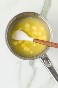 butter melting in a silver pan with a small white and wood handle spatula