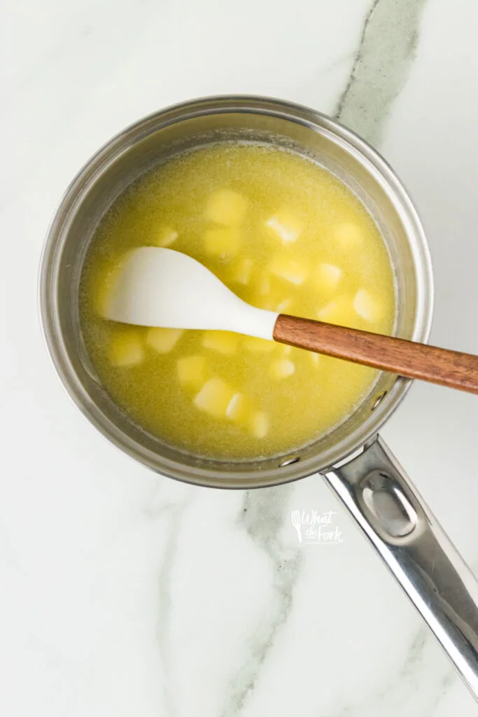 butter melting in a silver pan with a small white and wood handle spatula