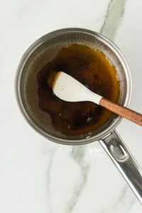 overhead shot of brown butter in a silver pan with a small white and wood handle spatula