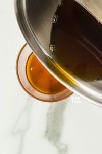 brown butter being poured from a silver saucepan into a glass bowl to cool