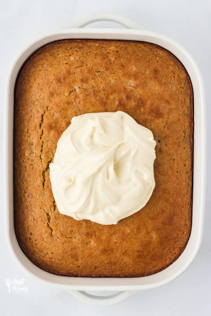 gluten free banana cake baked with a dollop of cream cheese frosting on top in a 9x13 white baking pan