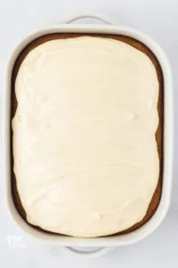 gluten free banana cake baked topped with cream cheese frosting in a white 9x13 baking pan